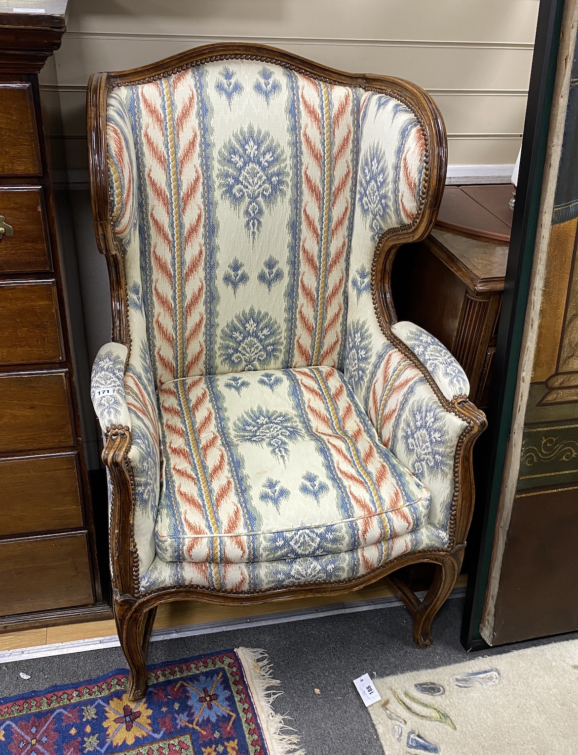 A Louis XV Provincial walnut wing armchair, with moulded frame, arched stuffed back loose cushion seat and cabriole legs joined by stretchers, width 63cm, depth 70cm, height 115cm